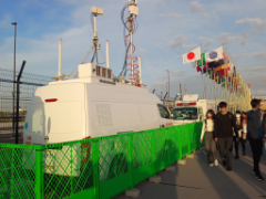"18:12 東ゲート外に並ぶ国旗と、キャリア各社の臨時局"